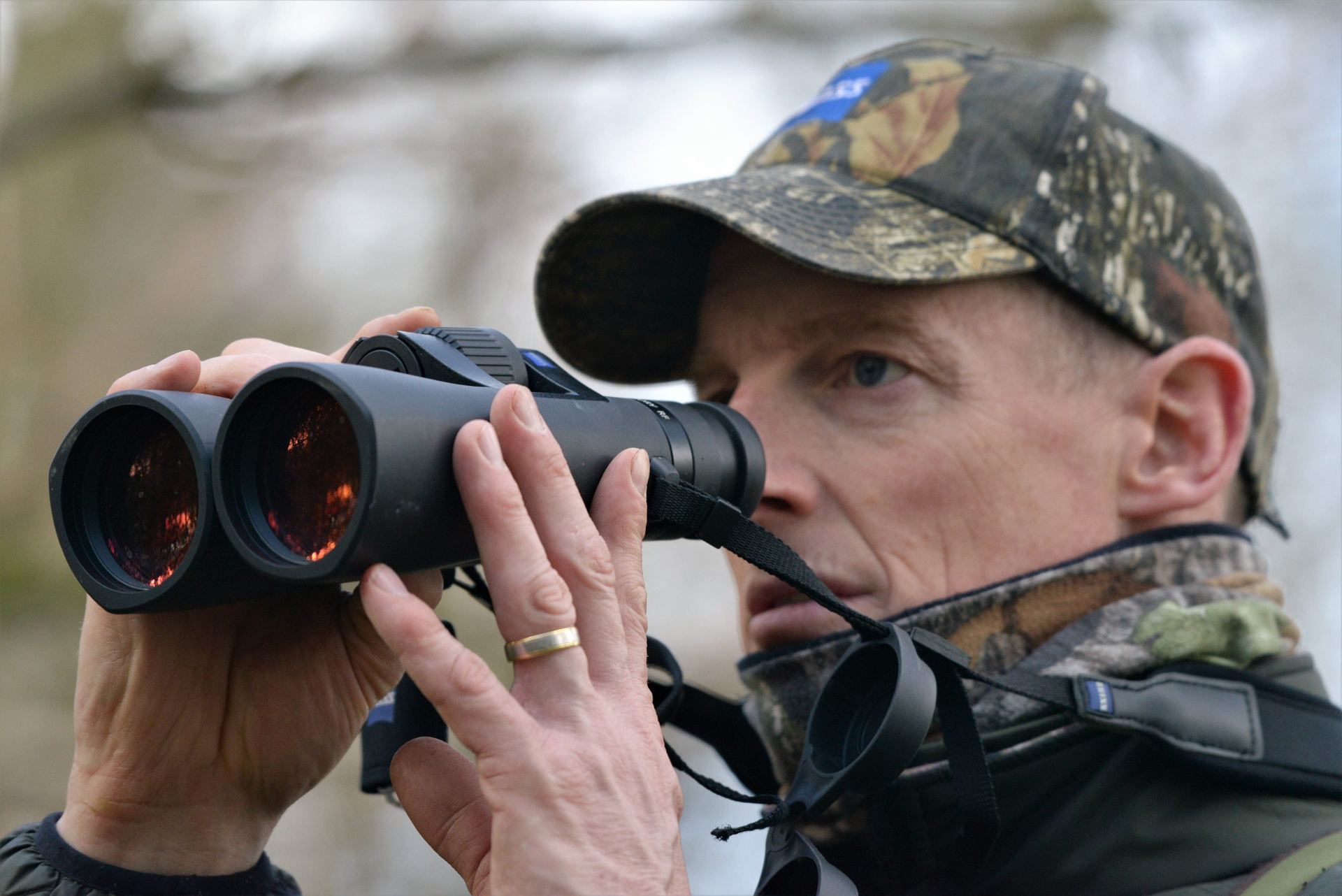 Hunter in a camo cap glassing through binoculars, close-up on the lenses.