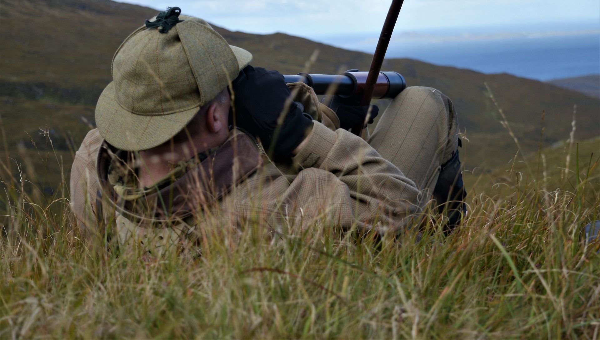 Hunter lying in the grass glassing across open hills before ranging a shot.
